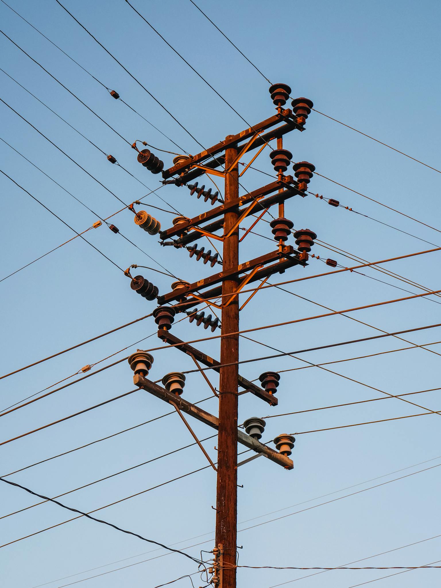 Close-up of a high voltage utility pole with transmission lines against a clear blue sky.